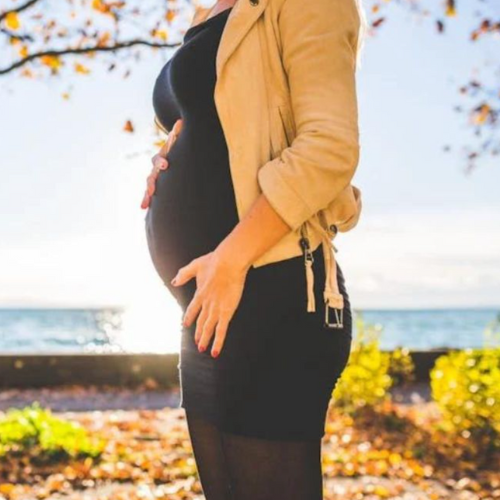 An image of a pregnant lady standing in front of the sea in autumn